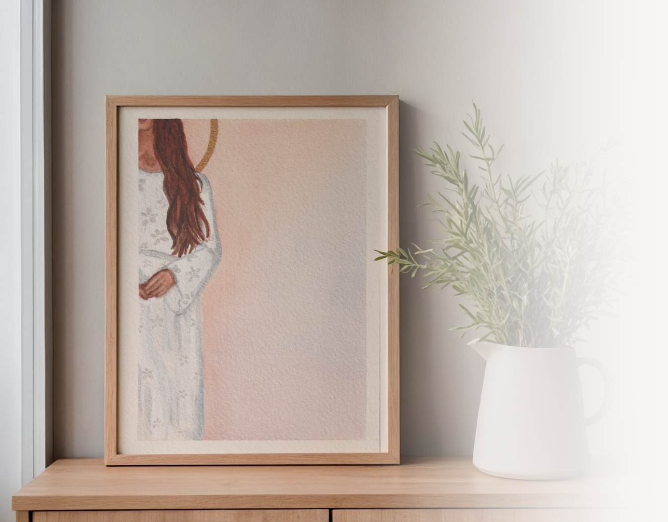 A framed watercolor art print depicting a woman in a white dress with long brown hair, leaning against a light gray wall on a wooden table next to a white pitcher vase with green branches.